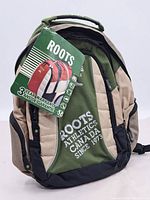 Front view of backpack with Roots tag showing warranty info and color details.