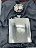 Polished metal flask with textured surface and matching funnel in a satin-lined padded case.