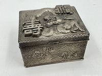 Overall angled view of the rectangular silver-tone jewelry/trinket box showing the dragon and Chinese characters on the lid and floral decorations on the side.
