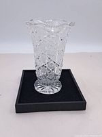Full view of clear crystal vase standing on black surface showing flared top and detailed cut patterns.