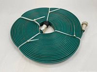 Overall view of coiled green garden hose with metal fittings at each end secured with zip ties