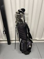 Full view of black Bullet golf bag with golf clubs inside, standing upright on a gray floor near a wall.