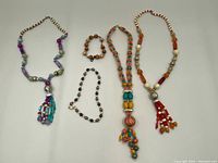 Group photo of 4 assorted bead necklaces and 1 bracelet on white background, showing variety of bead styles, strands and tassels