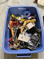 Plastic bin full of various hand tools and hardware including hammers, hand drill, pliers, screwdrivers, measuring tapes, wire rolls and boxed components.