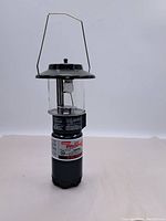 Full view of vintage Coleman propane lantern standing upright showing metal top, handle, glass globe, and propane base with label.
