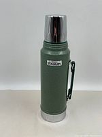 Front view of vintage green Aladdin Stanley thermos with silver cup lid and handle on white background