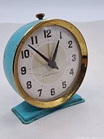 Front and side angle showing blue metal round casing and white dial with black numbers and hands.