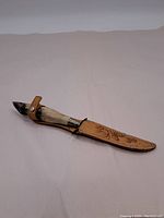 Photo of the knife sheathed in the decorated leather sheath, showing the unique deer hoof handle with fur and the sheath's tooling and snap closure.