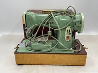 Side view of vintage green Singer sewing machine on carrying case with electrical cord wrapped on side.