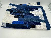 Photo of the quilt folded showing the patchwork pattern of blue and white fabric strips.