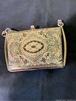 Front view showing ornate engraved metal exterior with floral and scroll detailing.