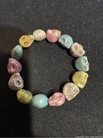 Photo shows round bangle bracelet made of multiple small skull-shaped beads in various pastel and earth tones against black background.
