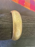 Close-up of the handmade brass bangle showing detailed floral and leaf engravings on outer surface.