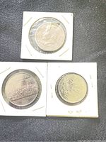 Three coins in holders: top coin with Queen Elizabeth II profile, bottom left coin with conservation imagery, bottom right coin with emblem design.