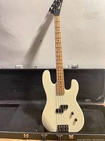 Front view of cream colored bass guitar in open hardshell case showing body, pickup, bridge and controls