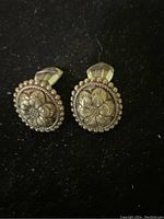 Front view of round silver-tone floral clip earrings with detailed embossed flowers and beaded border.