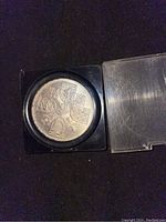 Silver coin showing shields representing parts of the UK in a protective display case