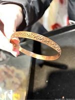 Copper bangle bracelet held in hand showing engraved floral decorative pattern.