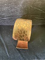 Close-up photo of one copper cuff bracelet showing the hammered textured surface pattern and open-ended design.
