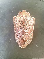 Close-up photo of copper cuff bracelet showing detailed floral engraving and scalloped edges.