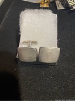 Pair of square silver cufflinks with fine dotted border, displayed on white foam in small box.