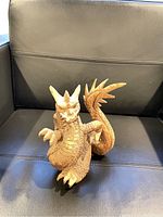 Wooden dragon figurine carved with detailed scales, claws, wings, and horns positioned upright on a black leather chair.