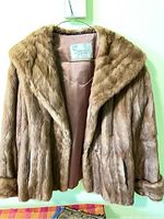 Front view of vintage fur coat with shawl collar, hanging on wall hook.