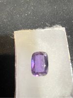 Close-up of purple rectangular faceted gemstone on dark background.