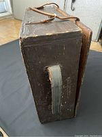 Side view of the wooden box showing leather handle attached to side and wear marks on wood.