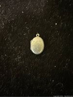 Photo showing a small silver heart-shaped locket resting on a dark surface, engraved details visible on the front.