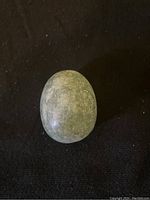 Polished green jade egg stone with smooth surface and natural color variations against a black background.