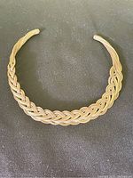 Copper braided necklace laid flat on a dark surface showing intricate braided design and smooth ends.