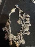 Full view of antique silver necklace showing layered chains and dangling leaf-shaped charms, along with triangular settings containing colored stones.