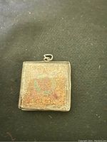 Front of the square silver pendant showing tarnished surface with mixed coloration and patina.