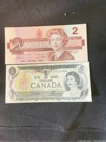 Front sides of Canadian 1 dollar and 2 dollar banknotes showing Queen Elizabeth II portraits and serial numbers.