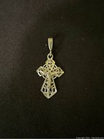 Single silver cross pendant with intricate Celtic knot design on a black background.