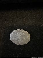 Front view of the vintage silver brooch showing detailed engraved floral and scrollwork designs on a scalloped oval surface.