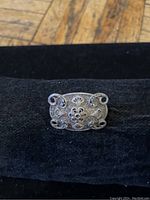 Front view of rectangular vintage silver brooch with detailed filigree floral and scrollwork design.