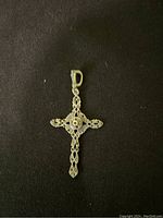 Photo of a silver cross pendant showing detailed filigree and central bead on a dark background