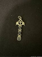 Close-up photo of a silver cross pendant with decorative elements on a dark fabric background.