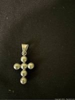 Close-up photo of a sterling silver cross pendant made of seven rounded beads with a silver bail on top for chain attachment