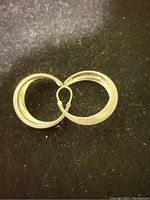 Close-up photo of one silver hoop earring showing textured diagonal lines detail and clasp mechanism.