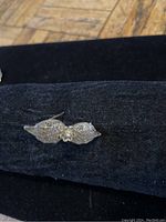 Photo of one vintage silver filigree earring displayed on black fabric, showing side angle and intricate openwork metal design