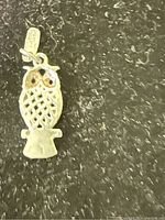 Close-up of the silver owl pendant showing detailed body lattice, eye accents, and hanging loop.