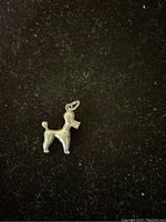 Clear image of a small silver pendant shaped like a dog or puppet on a black background