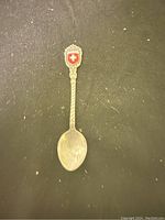 Photo shows a silver souvenir spoon with a twisted handle and Swiss crest on the top against a dark background.