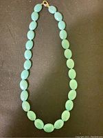 Full view of the turquoise beaded necklace laid flat on a black surface, showing the gold-toned clasp.