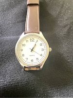 Front view of the quartz wrist watch showing the white dial, Arabic numeral hour markers, date window at 6 o'clock, and brown leather strap.