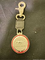 Front view of Ford Mustang keychain with red-bordered round emblem and Mustang logo on leather strap with metal clasp.