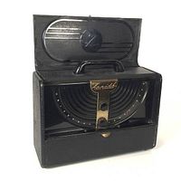 Front view with lid open showing curved semi-circular tuning dial with concentric circles, two black knobs on central brass strip engraved 'Zenith Long Distance', and speaker behind grille.